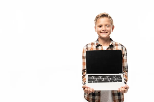 Веселий хлопчик показує ноутбук з порожнім екраном, посміхаючись на камеру ізольовано на білому — стокове фото