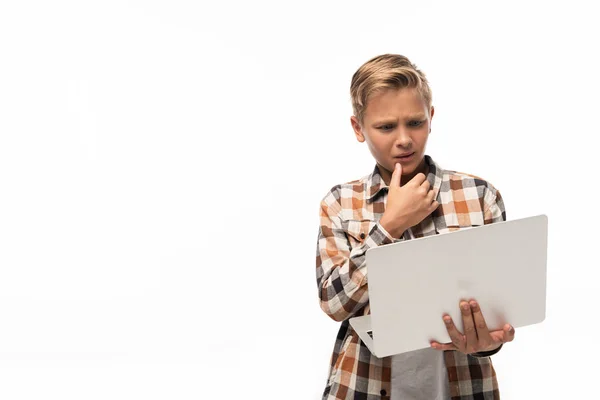 Задумливий хлопчик дивиться на ноутбук і тримає руку біля обличчя ізольовано на білому — стокове фото