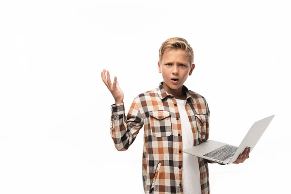 Обескураженный мальчик держит ноутбук, смотрит в камеру и показывает жест пожатия, изолированный на белом — стоковое фото