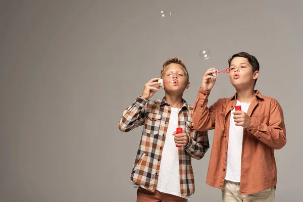 Deux mignons garçons soufflant des bulles de savon isolé sur gris — Photo de stock