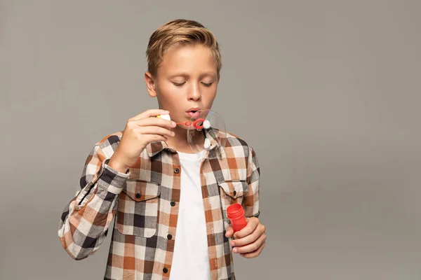 Cute boy blowing soap bubbles isolated on grey — Stock Photo