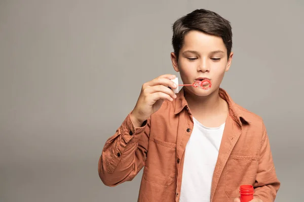 Cute boy blowing soap bubbles isolated on grey — Stock Photo