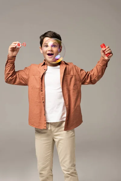 Amazed boy looking at soap bubble isolated on grey — Stock Photo