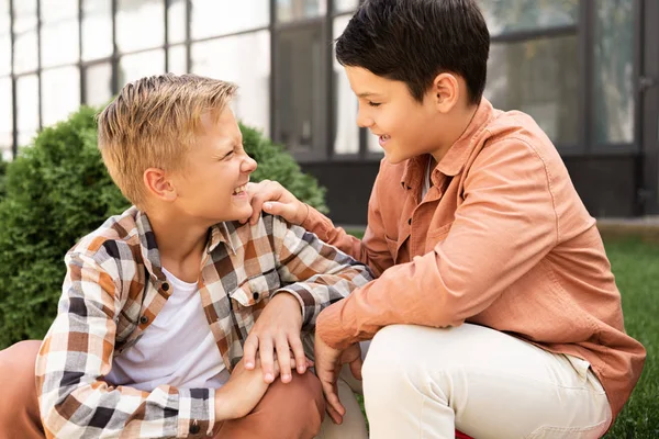 Dos hermanos felices mirándose y sonriendo mientras están sentados en la calle - foto de stock