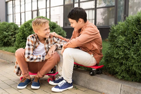 Cheerful brothers talking while sitting on pavement near green bushes — Stock Photo