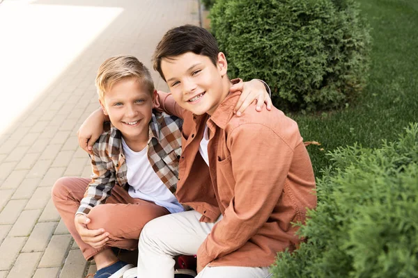 Dos hermanos alegres sonriendo sentados en el pavimento y mirando a la cámara - foto de stock