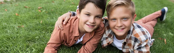 Scatto panoramico di due fratelli felici che sorridono alla macchina fotografica sdraiati sull'erba — Foto stock