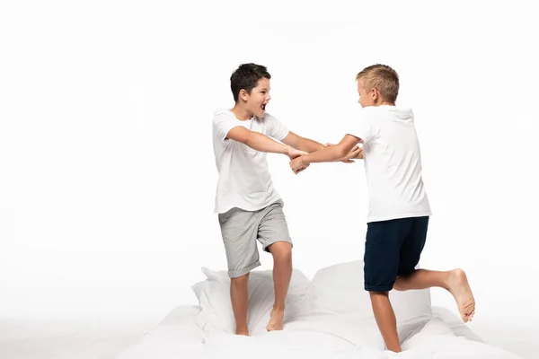Dois irmãos lutando por diversão branco de pé na cama isolado no branco — Stock Photo
