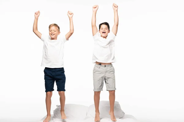 Dois irmãos alegres em pé na cama e mostrando gesto vencedor isolado no branco — Fotografia de Stock