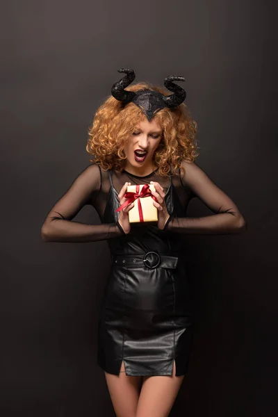 Assustador encaracolado mulher no maléfico traje segurando caixa de presente para halloween no preto — Fotografia de Stock