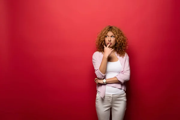 Beautiful pensive woman with red curly hair, isolated on red — Stock Photo