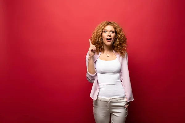 Beautiful redhead woman pointing up with idea, isolated on red — Stock Photo