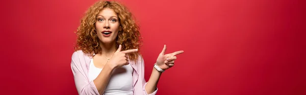 Attractive surprised redhead woman pointing isolated on red — Stock Photo