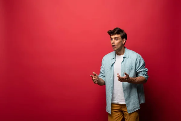 Handsome shocked man in casual clothes gesturing isolated on red — Stock Photo