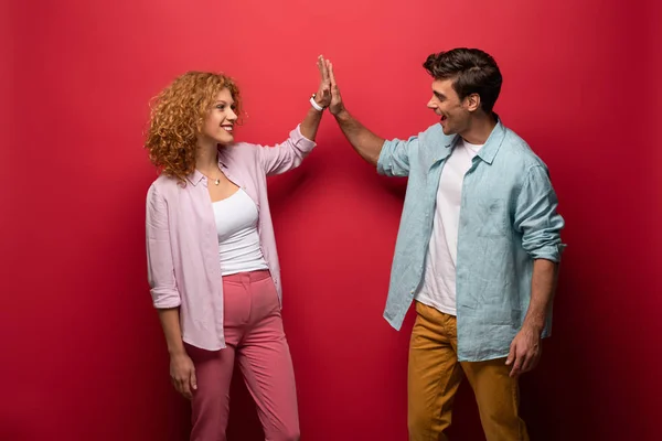 Beautiful happy couple in casual clothes giving high five, isolated on red — Stock Photo