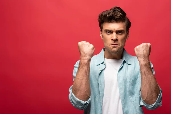 Retrato de homem com raiva em roupas casuais mostrando punhos isolados no vermelho — Fotografia de Stock