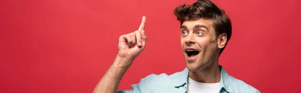 Portrait of handsome shocked man in casual clothes pointing up and having idea, isolated on red — Stock Photo