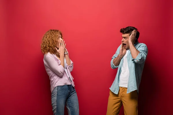 Beautiful scared couple looking at each other, isolated on red — Stock Photo