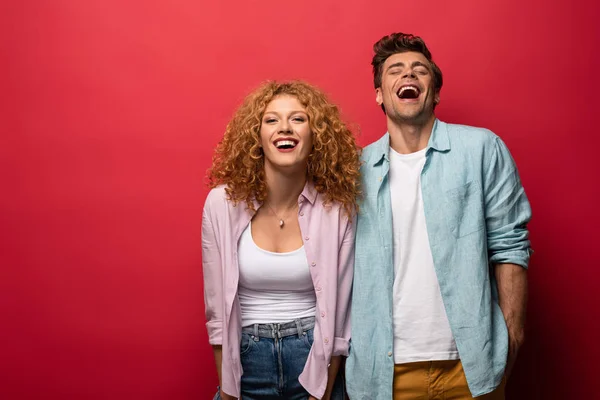 Beautiful happy couple in casual clothes laughing isolated on red — Stock Photo