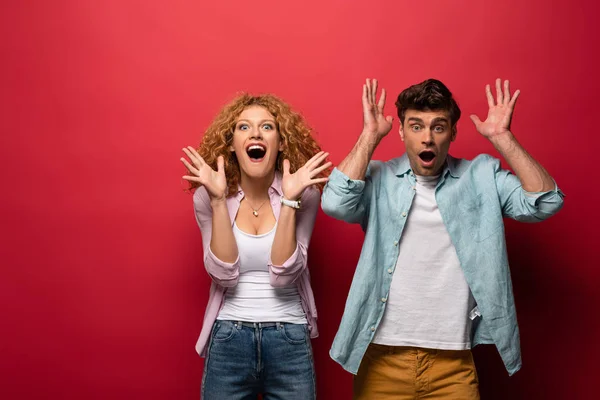 Excited woman and shocked man gesturing in casual clothes isolated on red — Stock Photo