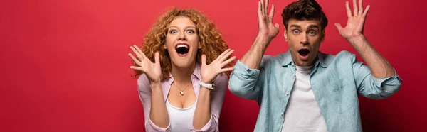 Pareja emocionada y conmocionada haciendo gestos en ropa casual aislada en rojo - foto de stock