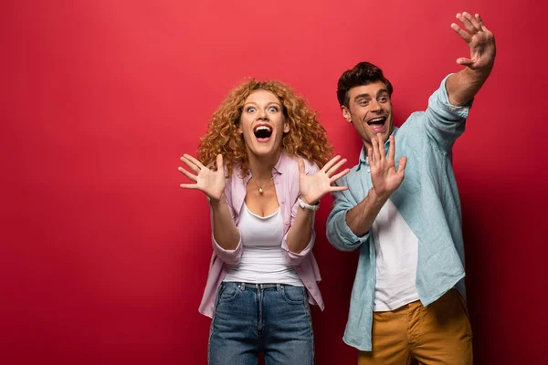 Beautiful excited couple gesturing in casual clothes isolated on red — Stock Photo