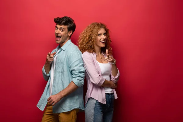 Belo casal animado mostrando apontando para você, isolado no vermelho — Fotografia de Stock