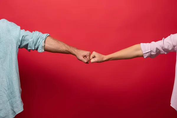 Partial view of couple bumping fists, isolated on red — Stock Photo