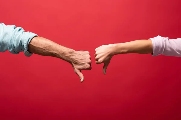 Partial view of young couple showing thumbs down, isolated on red — Stock Photo