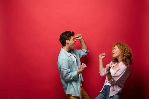 Belo casal animado celebrando triunfo, isolado no vermelho — Fotografia de Stock