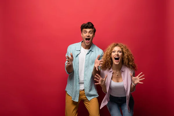 Beautiful shocked couple screaming and gesturing, isolated on red — Stock Photo