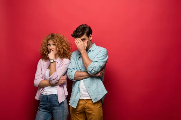 Young skeptical couple in casual clothes isolated on red — Stock Photo