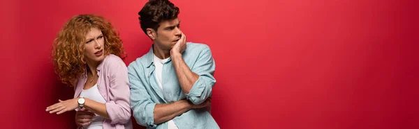 Hermosa pareja escéptica en ropa casual aislado en rojo - foto de stock