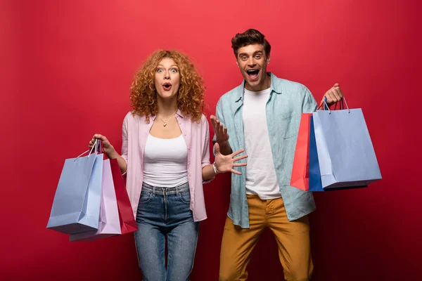 Excitada hermosa pareja sosteniendo bolsas de compras, aislado en rojo - foto de stock