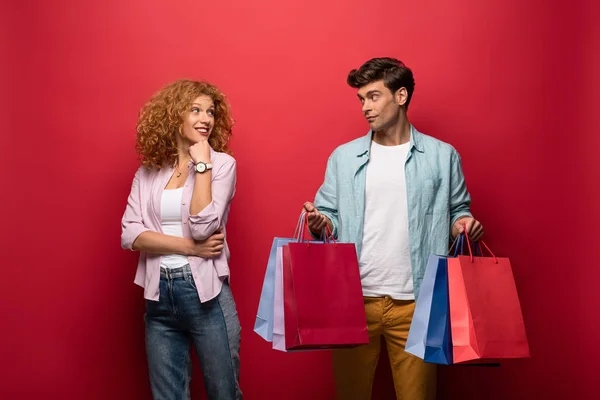 Schönes lächelndes Paar mit Einkaufstaschen, isoliert auf rot — Stockfoto