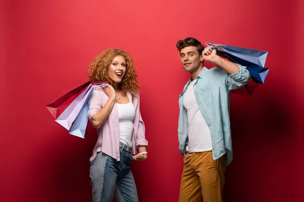 Casal alegre segurando sacos de compras, isolado no vermelho — Fotografia de Stock