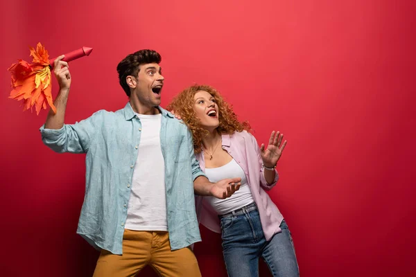 Beau couple excité lancer petite fusée, sur rouge — Photo de stock