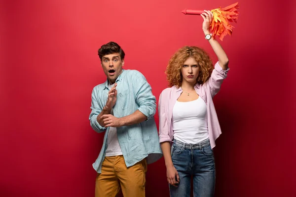 Curly confident woman holding little rocket near scared man, on red — Stock Photo