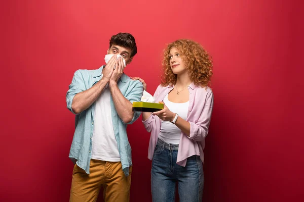 Woman and diseased man with runny nose holding paper napkins, on red — Stock Photo