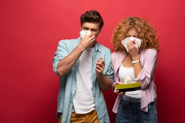 Sad diseased couple with runny nose holding paper napkins, on red — Stock Photo