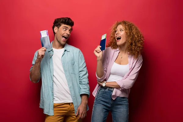 Viajeros excitados sosteniendo pasaportes con boletos aéreos, aislados en rojo - foto de stock