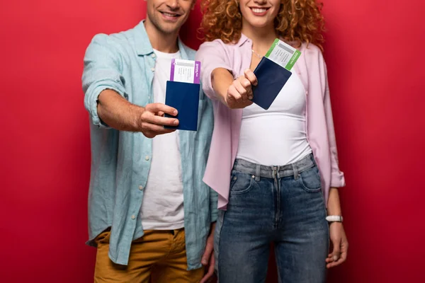 Vista recortada de viajeros sonrientes que muestran pasaportes con boletos aéreos, aislados en rojo - foto de stock