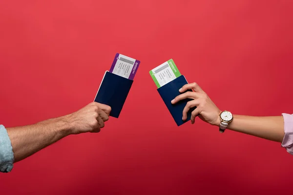 Vista cortada de viajantes segurando passaportes com passagens aéreas em mãos, isolado em vermelho — Fotografia de Stock