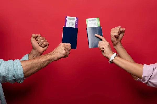 Partial view of travelers holding fists and passports with air tickets, isolated on red — Stock Photo
