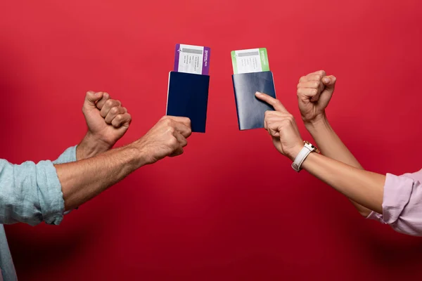 Vista parcial de viajeros sosteniendo puños y pasaportes con pasajes aéreos, aislados en rojo - foto de stock