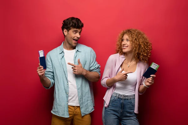 Viajantes excitados apontando para passaportes com passagens aéreas, isolados em vermelho — Fotografia de Stock