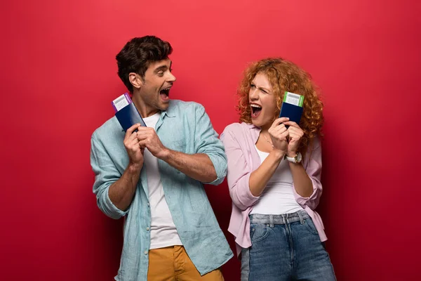 Pareja de viajeros emocionados sosteniendo pasaportes con billetes de avión, aislados en rojo - foto de stock