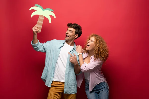 Paar glücklicher Reisender mit Papierpalme, isoliert auf rotem Grund — Stockfoto