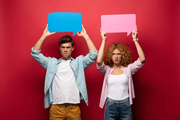 Angry couple holding pink and blue speech bubbles, on red — Stock Photo