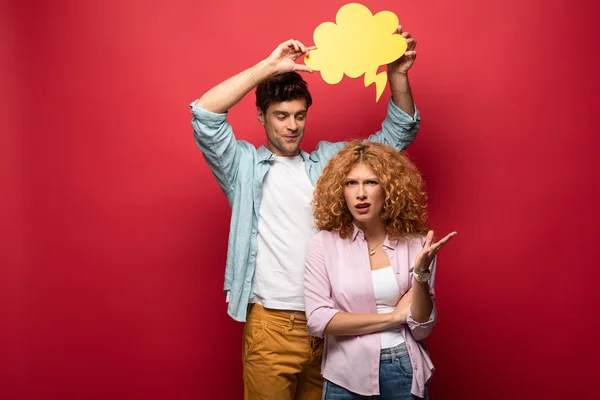 Boyfriend holding yellow cloud bubble over quarreling girlfriend, on red — Stock Photo